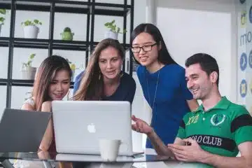 four people watching on white MacBook on top of glass-top table